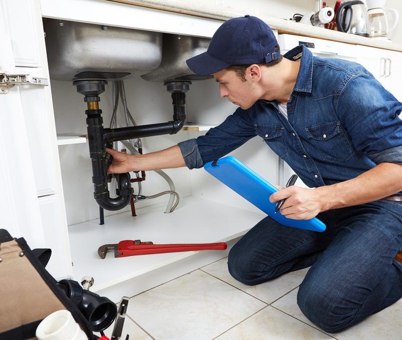 Plumber inspecting kitchen sink plumbing under cabinet