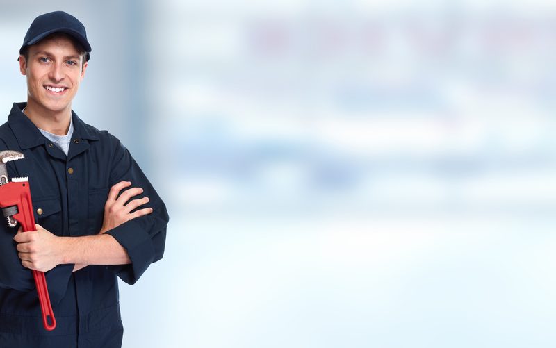 Smiling plumber holding a wrench in workshop.